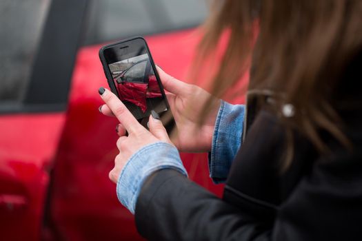 Woman using a smart phone to take a photo of the damage to her car caused by a car crash