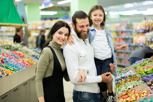A young family with a little girl choose candy and chocolate in a large store, supermarket.