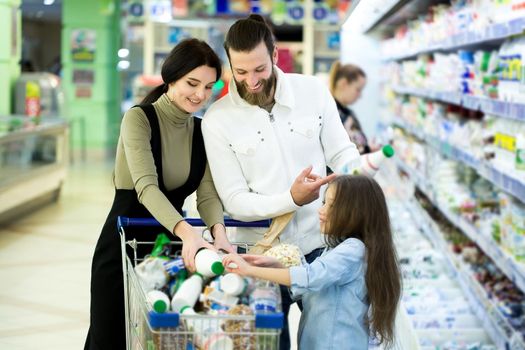 Young family with kid are choosing milk in supermarket.