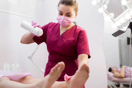Cosmetologist sprinkles talcum powder on a young girl's leg before the depilation procedure. The girl lies on a couch in a beauty salon, she does the procedure shugaring