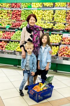 An old woman, a grandmother with grandchildren choose vegetables and fruits in a large supermarket.