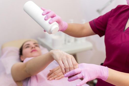 Close-up of a beautician sprinkles talcum powder on a young girl's hand before the depilation procedure. The girl lies on a couch in a beauty salon, she does the procedure shugaring