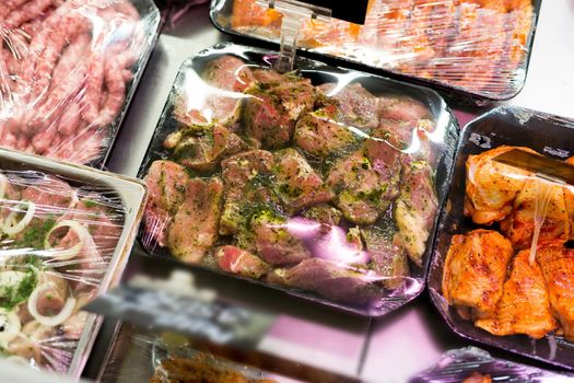 Meats in marinade on supermarket display, pre-cooked food