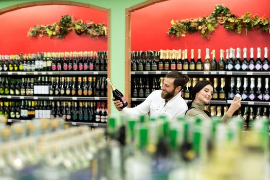 A young family, a man and a woman choose alcohol in a large supermarket.