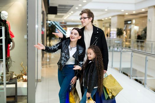 Happy young family with paper bags shopping at the Mall. Shop Windows with clothes