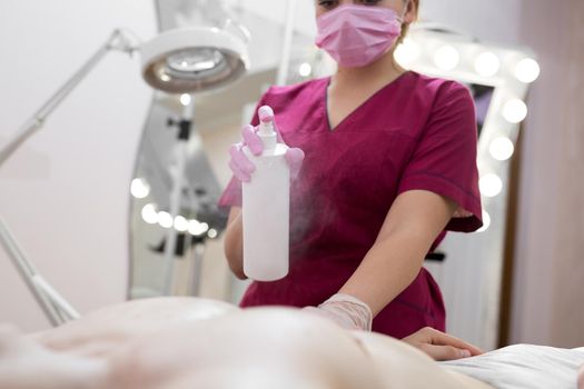 Close-up of mens Breasts in the beauty salon for the procedure of sugar hair removal. Beautician sprays disinfectant solution on the man's chest. Sugaring