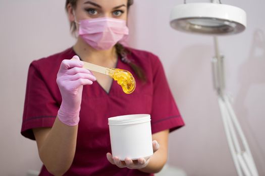 Cosmetician takes the sugar paste from the jar. Shugaring. Sugar paste out of the container with a spatula. Sugar paste for sugaring. Sugaring in beauty salon