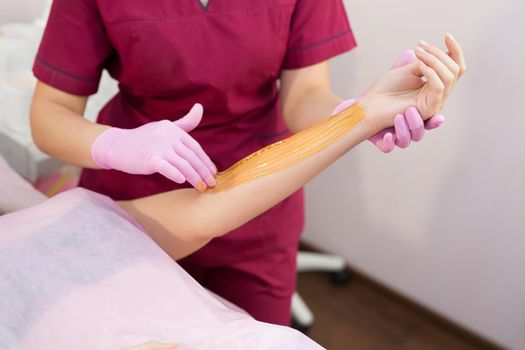 Sugaring. Beauty Concept. Young beautiful girl with dark hair gets the procedure for hair removal liquid sugar. Depilation and beauty concept - procedure of hair removing on hand on a beautiful woman
