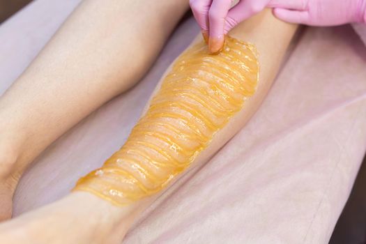 Sugar depilation of the feet in the beauty salon. Rid of hair on the legs. Sugaring. Master shugaring applies thick sugar paste on the legs of a young girl, removing hair on the legs. Close-up.