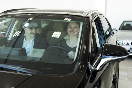 Agent and buyer girl inside a car in a car dealership. The seller shows the car to the buyer.
