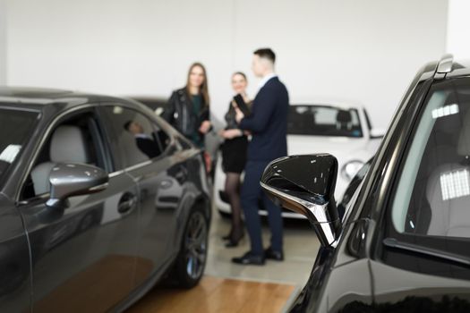 Auto business, car sales - a couple of friends of girls with a car dealer choose a car in a car dealership