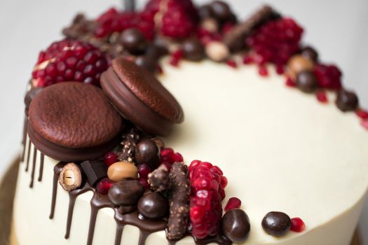 cake with white cream, chocolate drips, pomegranate, nuts and chocolate decor