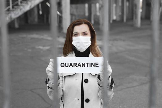 A woman behind bars in isolation holds a placard reading quarantine. Message for the prevention of coronavirus covind-19