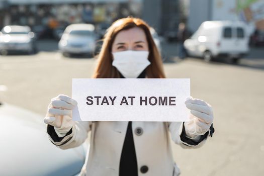 Woman in protective medical mask hold a placard reading stay at home. Message for prevention of bovine coronavirus-19