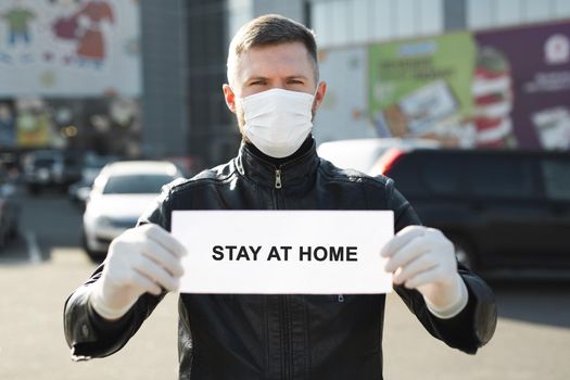 Man in protective medical mask hold a placard reading stay at home. Message for prevention of bovine coronavirus-19.