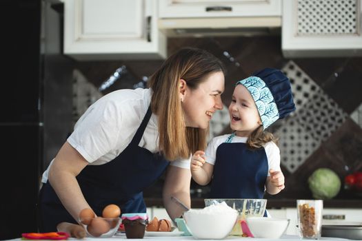 Young mother and daughter in the kitchen preparing cupcakes and smiling, laughing.