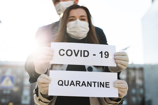 A woman and a man in protective medical masks hold a placard with the words Quarantine and Covid 19.