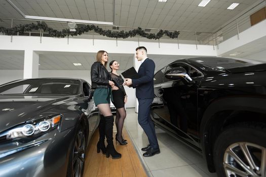 Auto business, car sales - a couple of friends of girls with a car dealer choose a car in a car dealership