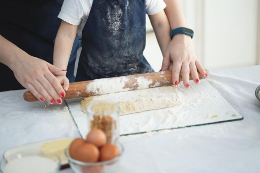 Mother and daughter roll out the dough with a rolling pin. Close-up view