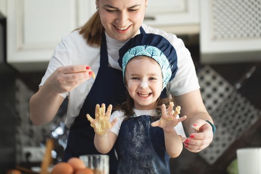 Mother and funny daughter showing hands in dough on kitchen