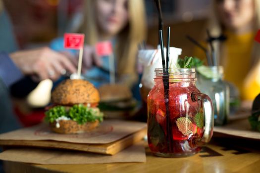Burger and cocktail on a wooden table in a restaurant close-up.