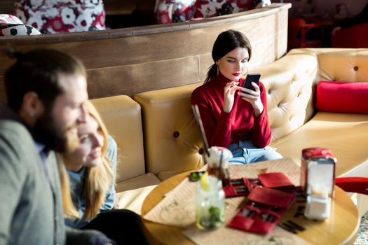 Friends are having dinner at a restaurant. A young couple hugs, and the woman is bored and looks at the phone.