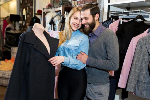 A young family, a man and a woman hug and choose a black coat in a clothing store.