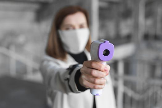 Coronavirus symptoms, woman in medical mask measures body temperature. Doctor looks at digital isometric non-contact thermometer in her hands, concept of covid-19 quarantine.