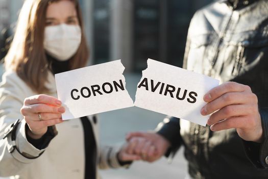 Masked man and woman tear up a paper labeled Coronavirus and hold hands.