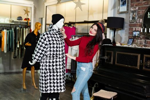 Joyful young woman shopping warm jackets at the apparel store. Shopping, fashion, clothes, style and people concept - happy woman trying coat on in mall or clothing store