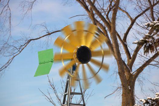 A small Windmill or Wind Turbine in a Rural Setting with Spinning Blades. Windmill has sunflower colors of yellow brown and green. High quality photo