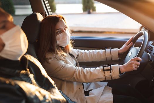 A man and a woman wearing medical masks and rubber gloves to protect themselves from bacteria and viruses while driving a car. The woman behind the wheel. Coronavirus, Covid-19.