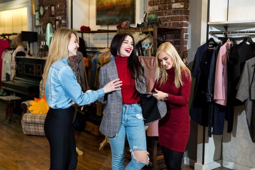 Shopping, fashion and friendship-three smiling friends try on clothes, a jacket in a shopping center.