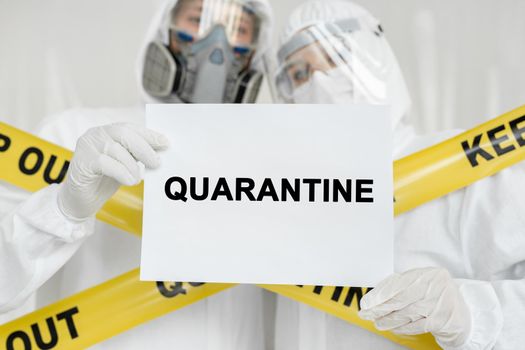 Doctors epidemiologists man and woman holding poster with sign Quarantine over white background. Yellow line Keep Out Quarantine.