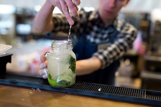 The bartender crushes ice for a Mojito cocktail on the bar.