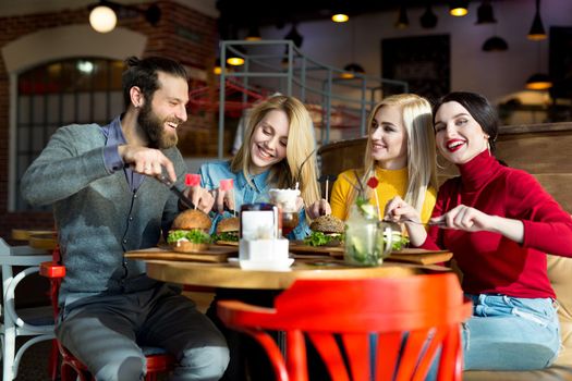 People have dinner together at a table in a cafe. Happy friends eat burgers and drink cocktails in the restaurant.