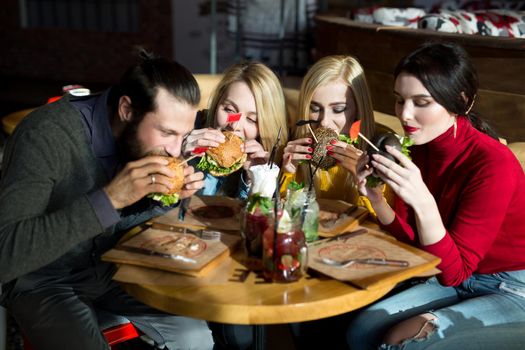 People have dinner together at a table in a cafe. Happy friends eat burgers and have fun.