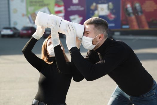 A woman and a man in a coronavirus face mask hold large rolls of toilet paper on a city street and indulge.