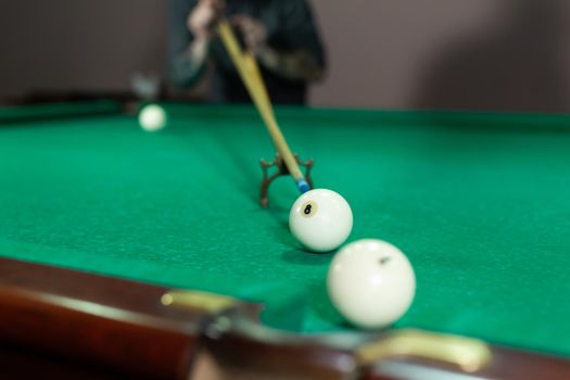 Man's hand and Cue arm playing snooker game or preparing aiming to shoot pool balls on a green billiard table