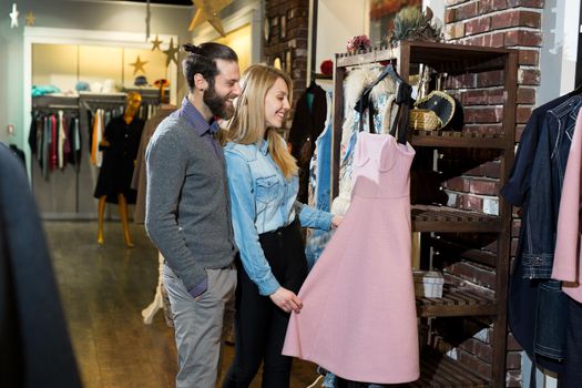 A young family, a man and a woman hugging and choosing a pink dress in a clothing store.