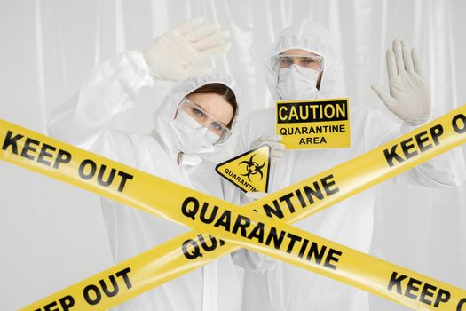 Epidemiologists a man and a woman in protective clothing are in a restricted area with a danger sign. Yellow line Keep Out Quarantine. Quarantine alert sign. Entrance is forbidden in quarantine zone