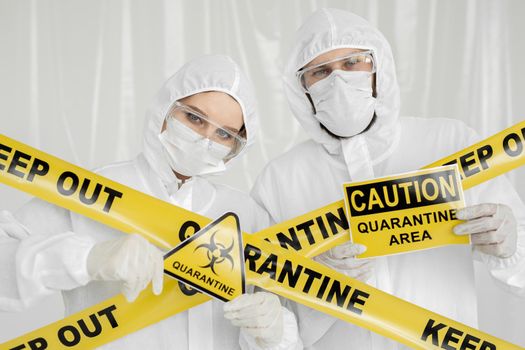 Epidemiologists a man and a woman in protective clothing are in a restricted area with a danger sign. Yellow line Keep Out Quarantine. Quarantine alert sign. Entrance is forbidden in quarantine zone.