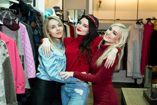 Shopping, fashion and friendship concept - three smiling friends trying on some clothes at shopping mall.