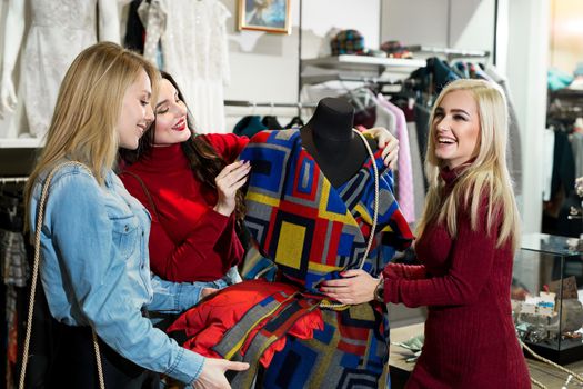 Shopping, fashion and friendship concept - three smiling friends trying on some clothes at shopping mall.