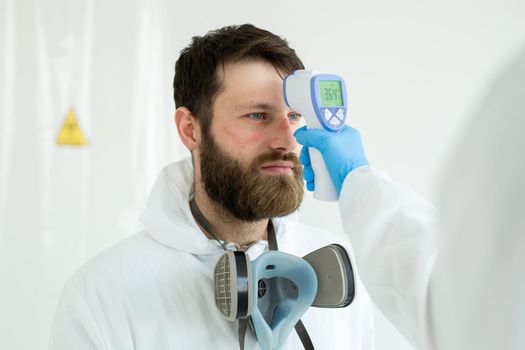 Doctor measures the temperature with an infrared thermometer to his colleague of infectious diseases. Portrait of a man doctor scientist in a lab coat. Concept of coronavirus.