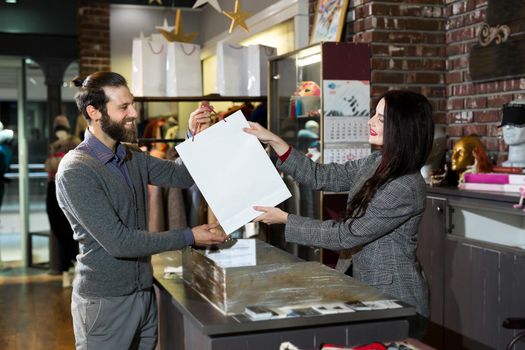 Attractive saleswoman, handing over a bag of clothes to a beautiful couple of men and women