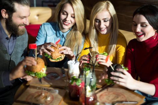 People have dinner together at a table in a cafe. Happy friends eat burgers and drink cocktails in the restaurant.