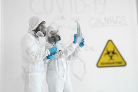 Doctors Epidemiologists examine x-ray for pneumonia of a Covid-19 patient. Coronavirus concept. Doctor in PPE suit uniform calculates the virus formula.