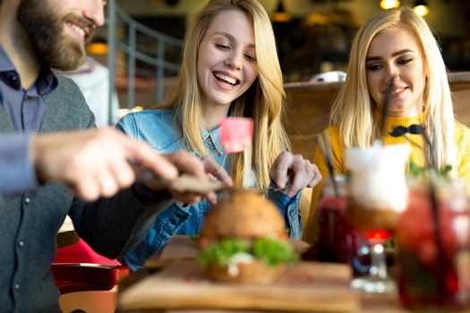 Happy friends cut a Burger with a knife in a restaurant and laugh.