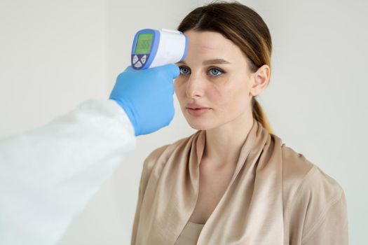 Doctor using an infrared thermometer to measure her patient's temperature in a clinic, a medical health concept